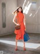 A woman in an orange dress holding a blue bag.