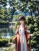 A woman in a traditional chinese dress standing in front of a lake.