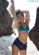 A woman in a blue bikini top and denim shorts on the beach.