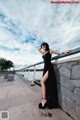 A woman in a black dress leaning against a stone wall.