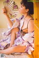 A woman in a kimono sitting on a bed holding a fan.