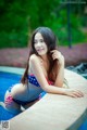 A woman in a bikini sitting on the edge of a pool.