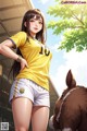 A woman in a yellow shirt and white shorts standing next to a brown horse.