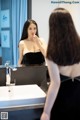 A woman in a black dress brushing her teeth in front of a mirror.