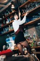 A woman standing in front of a bar holding a glass.