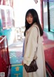 A woman in a white coat is standing in front of a bus.